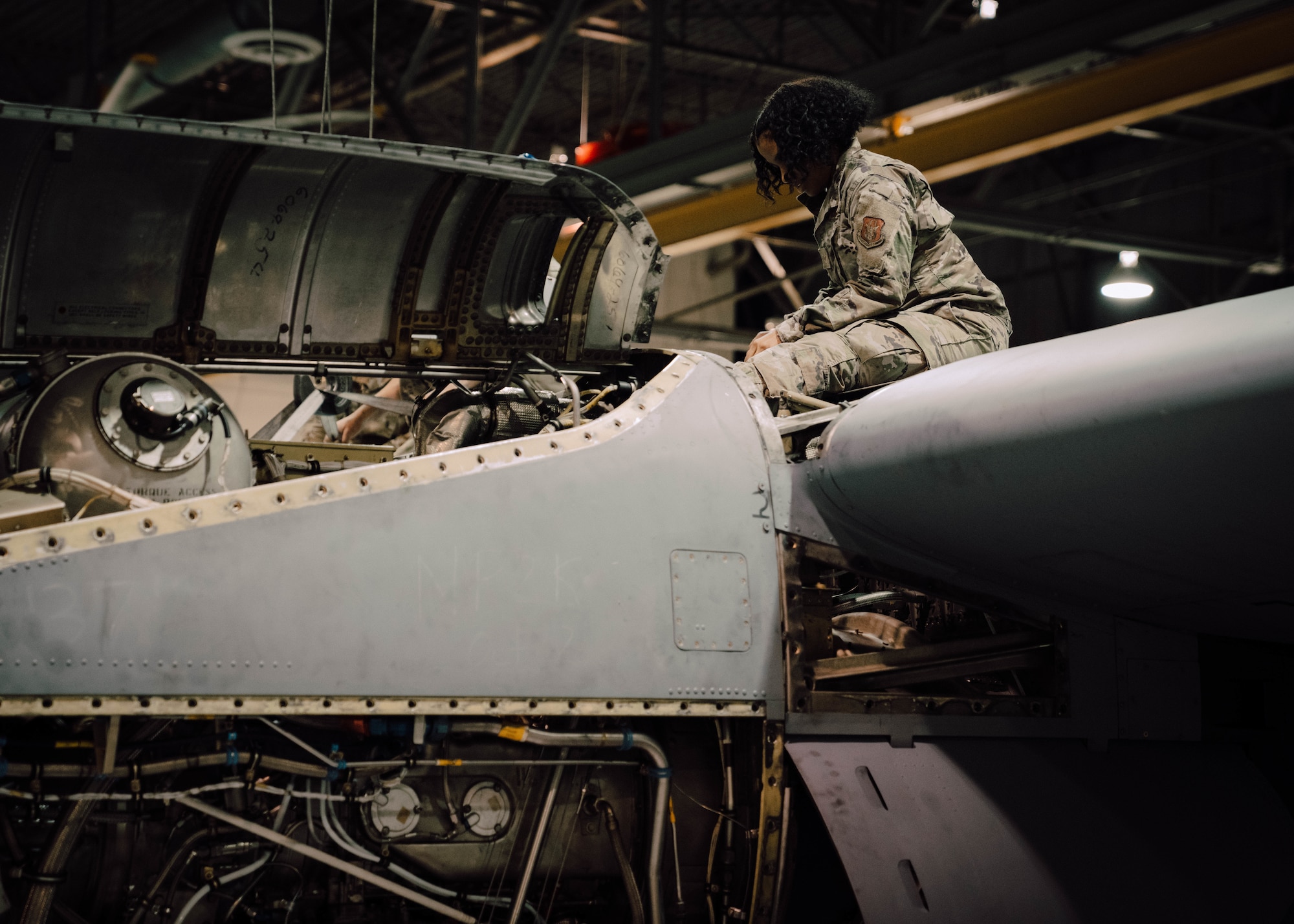 a person in military uniform perform maintenance on an aircraft