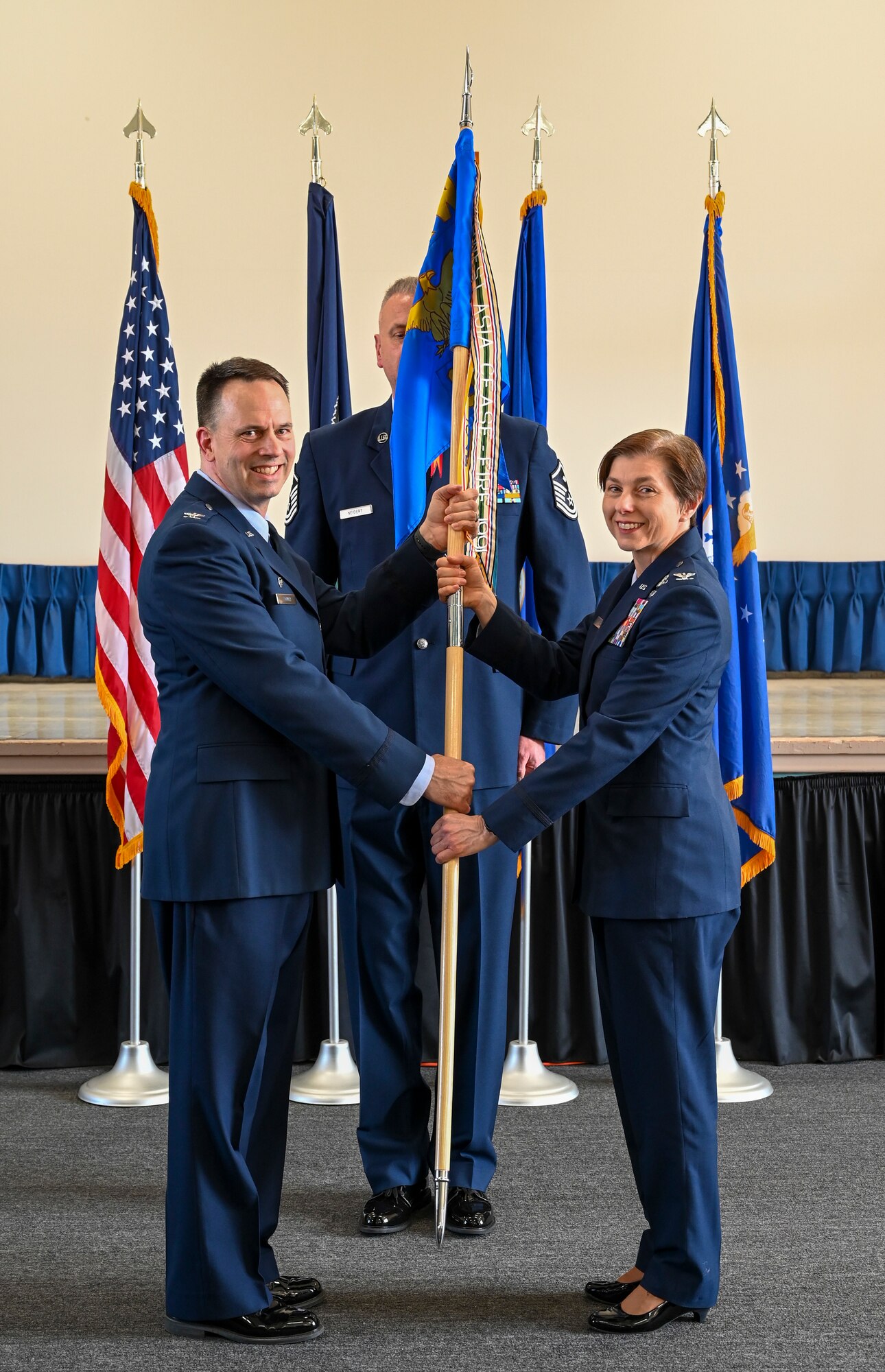 A man in Air Force dress blues hands a flag to a woman wearing Air Force dress blues.