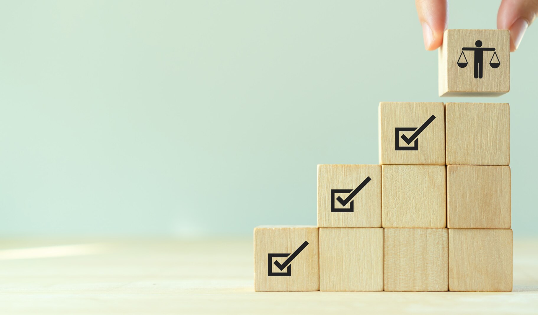 Integrity concept image. Wooden blocks with checkmarks images stacked like stairs with a hand placing the final top block with an image of balanced scales. Photo: © Parradee/stock.adobe.com [image is not public domain]