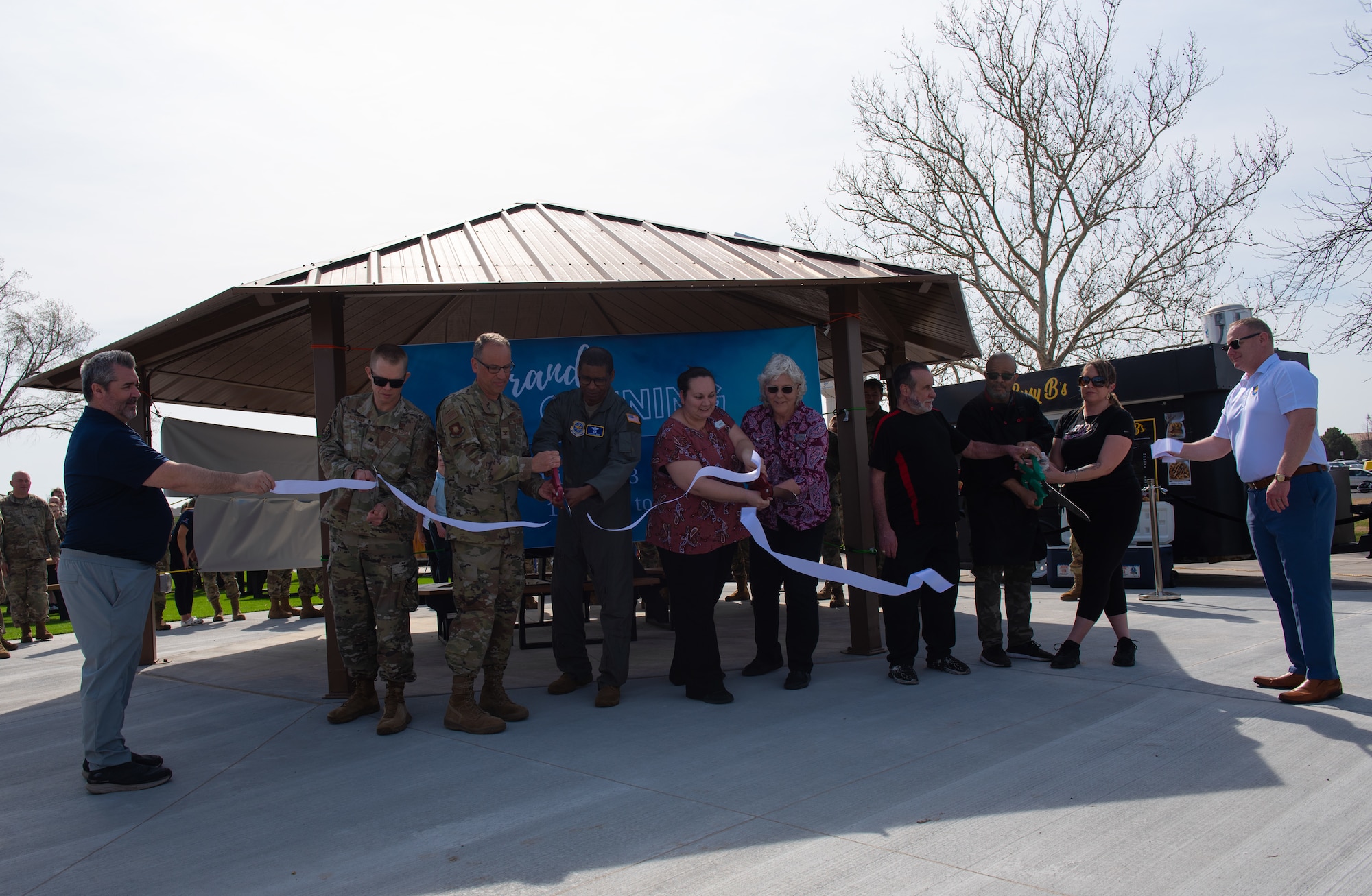 Leaders from the 22nd Air Refueling Wing, Air Mobility Command and Army and Air Force Exchange Service cut a ribbon at the grand opening for the food truck park at McConnell Air Force Base, Kansas, April 4, 2023. The food truck park provides a variety of easily accessible food for Team McConnell servicemembers. The area was designated a no hat, no salute area for the grand opening. (U.S. Air Force photo by Staff Sgt. Tryphena Mayhugh)