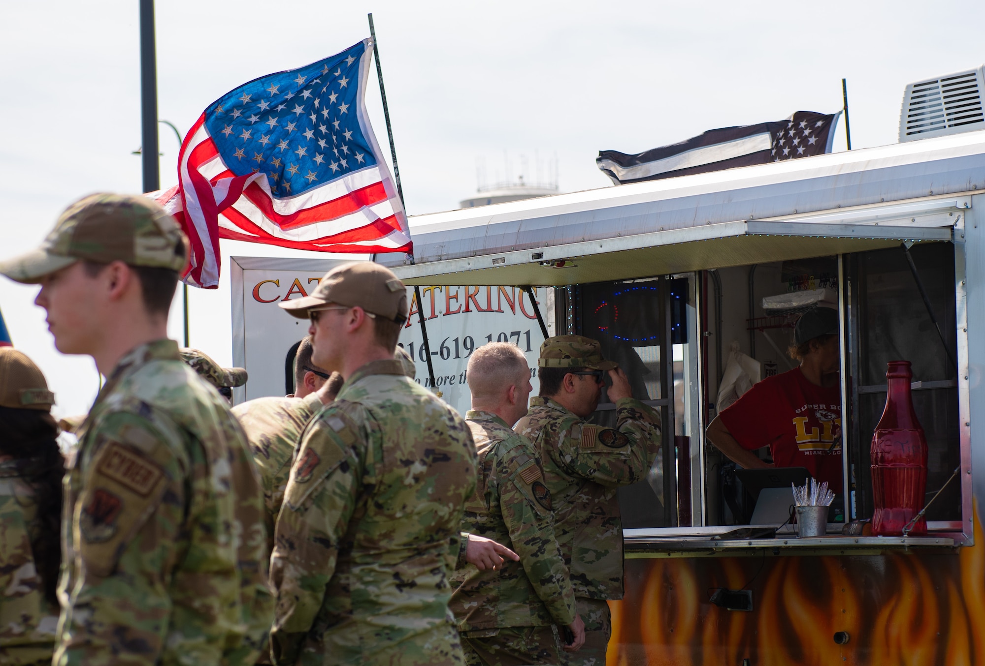 Team McConnell Airmen wait in line to order food at the grand opening for the food truck park at McConnell Air Force Base, Kansas, April 4, 2023. The food truck park provides a variety of easily accessible food for Team McConnell servicemembers. The area was designated a no hat, no salute area for the grand opening. (U.S. Air Force photo by Staff Sgt. Tryphena Mayhugh)