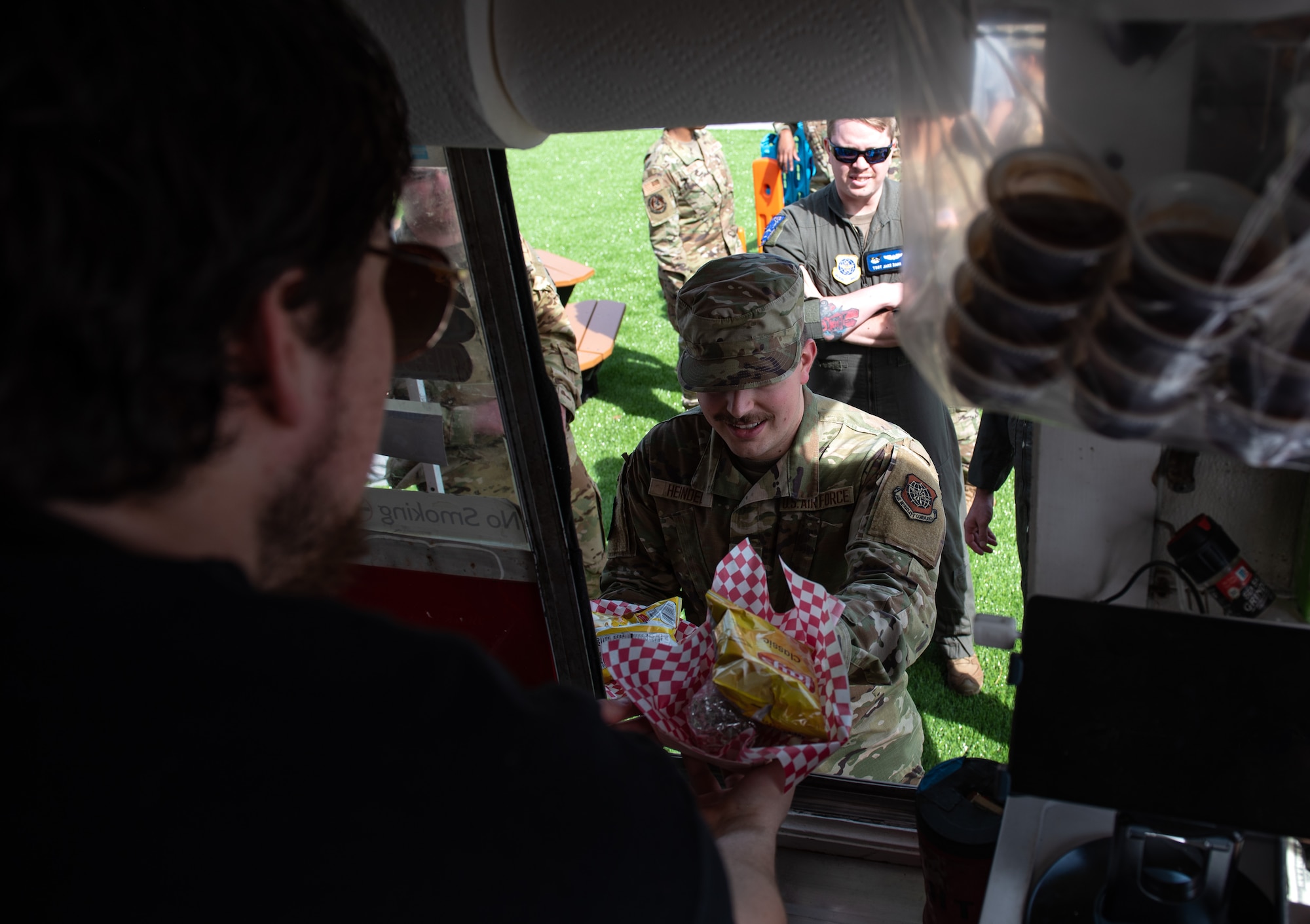 A Team McConnell Airman receives his food from a food truck employee during the grand opening for the food truck park at McConnell Air Force Base, Kansas, April 4, 2023. The food truck park provides a variety of easily accessible food for Team McConnell servicemembers. (U.S. Air Force photo by Staff Sgt. Tryphena Mayhugh)