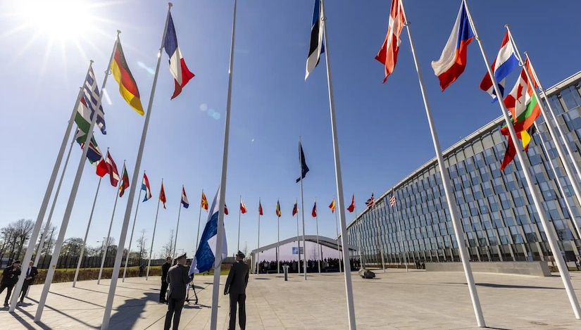 Three people in military dress uniform stand in the middle of a circle of flags.