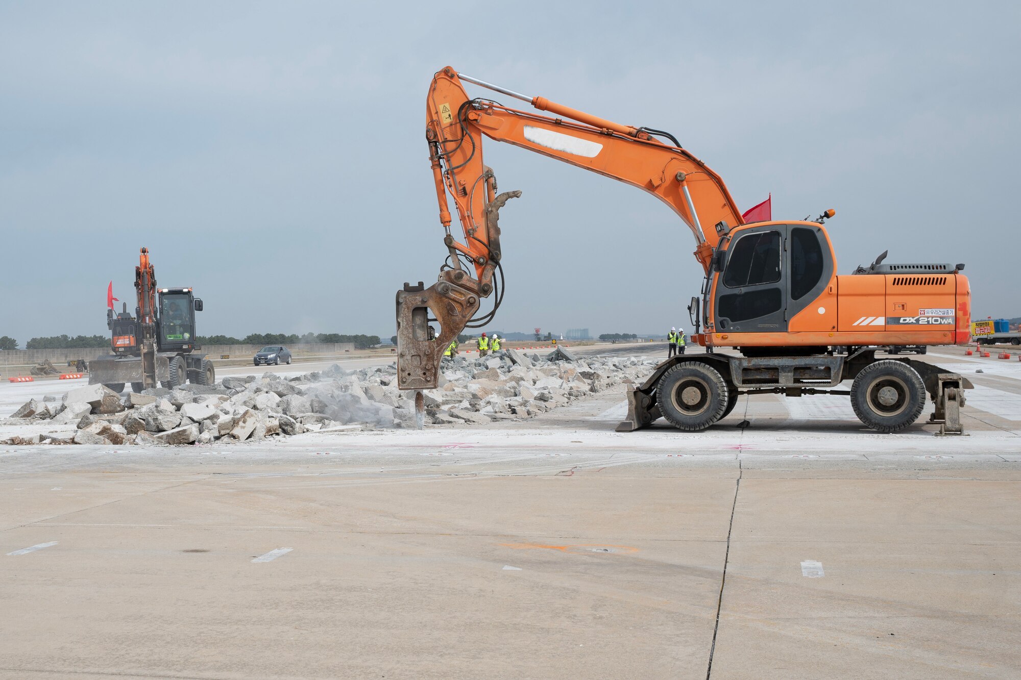 Excavators hammer concrete slabs on the runway.