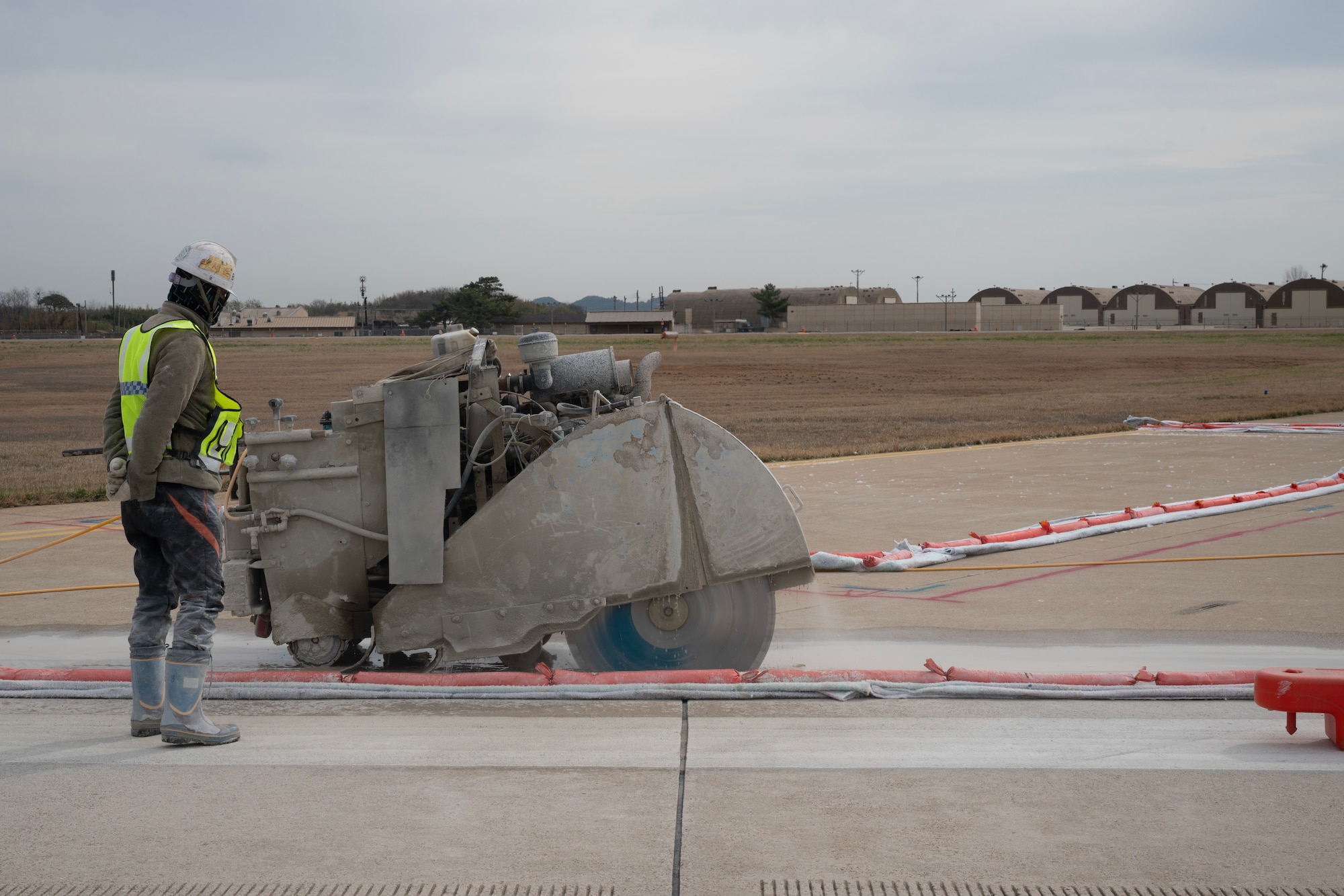 A Republic of Korea contractor watches a diamond blade concrete saw cut through concrete on a runway.