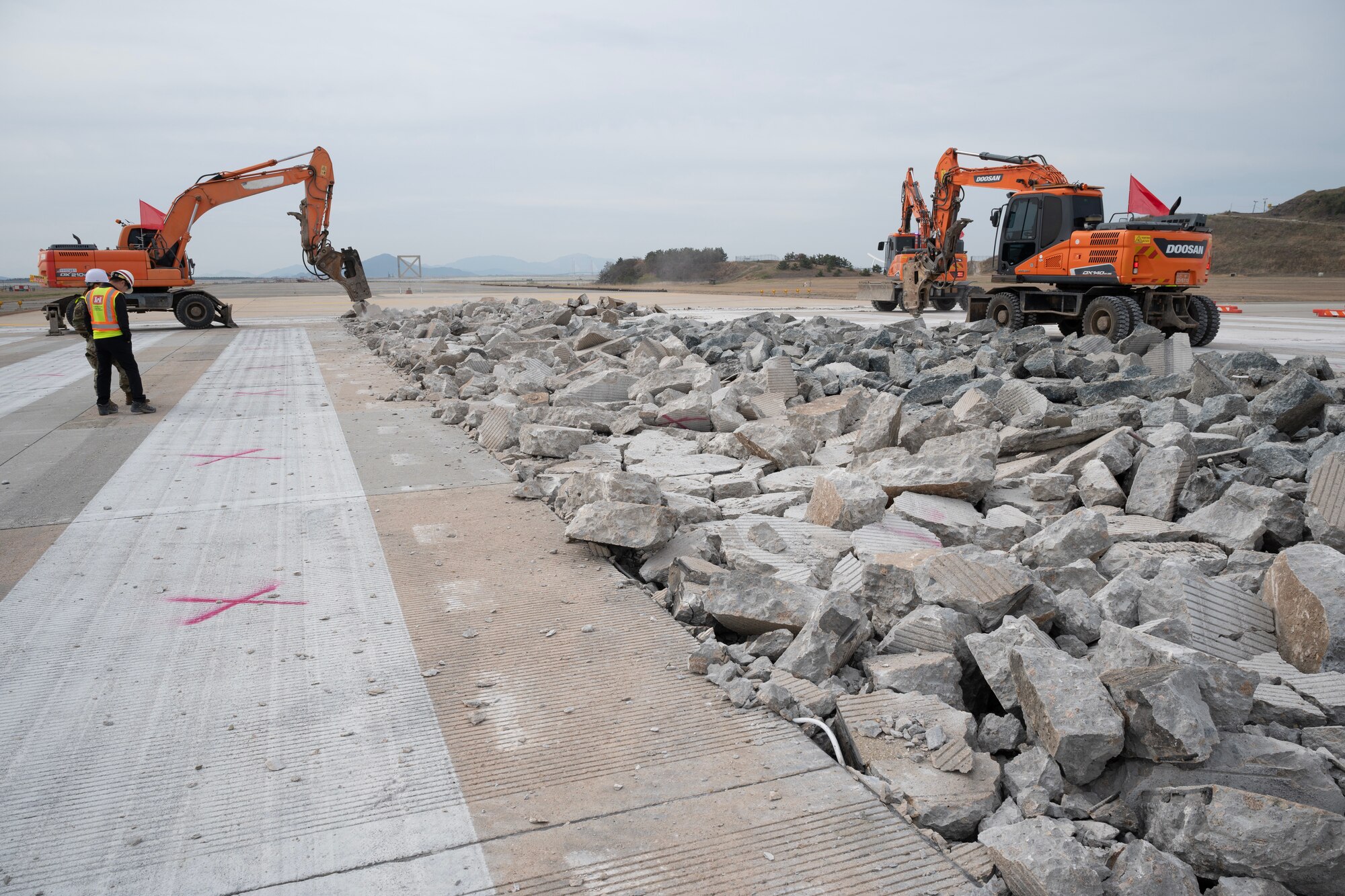 Excavators hammer concrete slabs on a runway.
