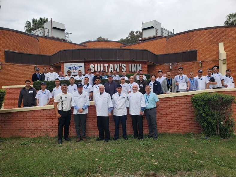 Team of about 30 pose in front of a building