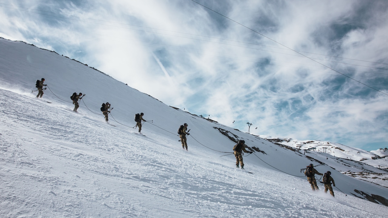 Soldiers ski in a line connected by a rope to each other.