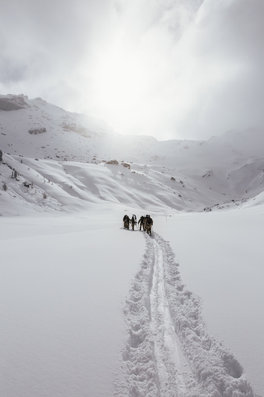 Soldiers travel in a line in the distance on skis, creating a powdery trail,