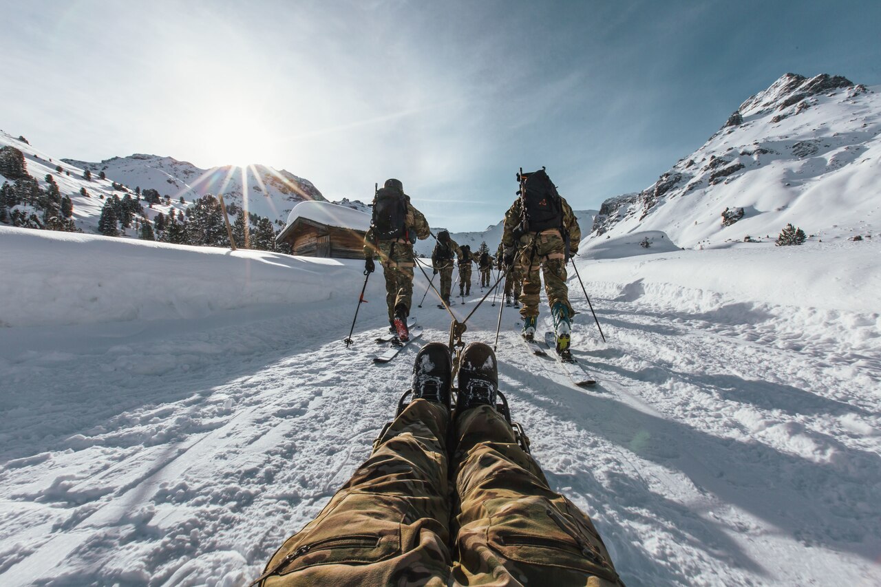 View of the backs of two lines of skiers dragging by ropes someone lying on a litter.