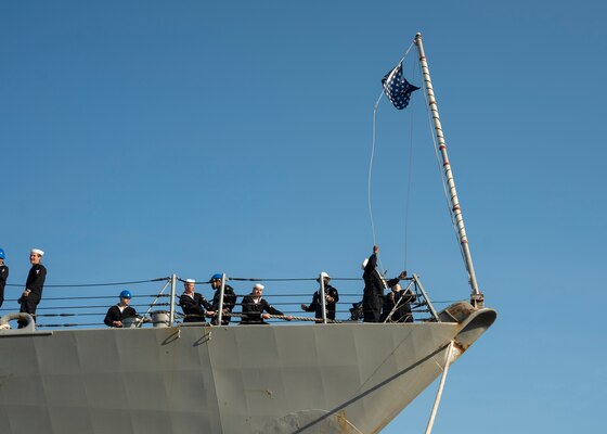 A Sailor aboard the guided-missile destroyer USS Nitze (DDG 94) raises the Union Jack as Nitze moors at Naval Station Norfolk after a scheduled deployment April 5, 2023.