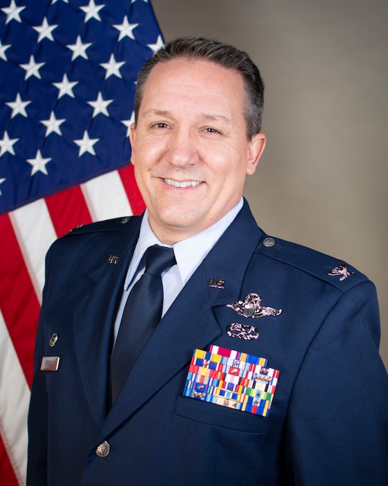 military member smiles in front of U.S. Flag for official portrait.