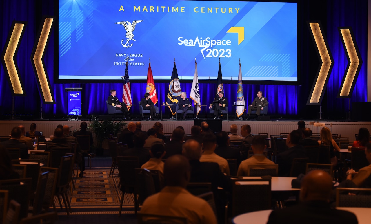 Five people sit on a platform facing an audience.