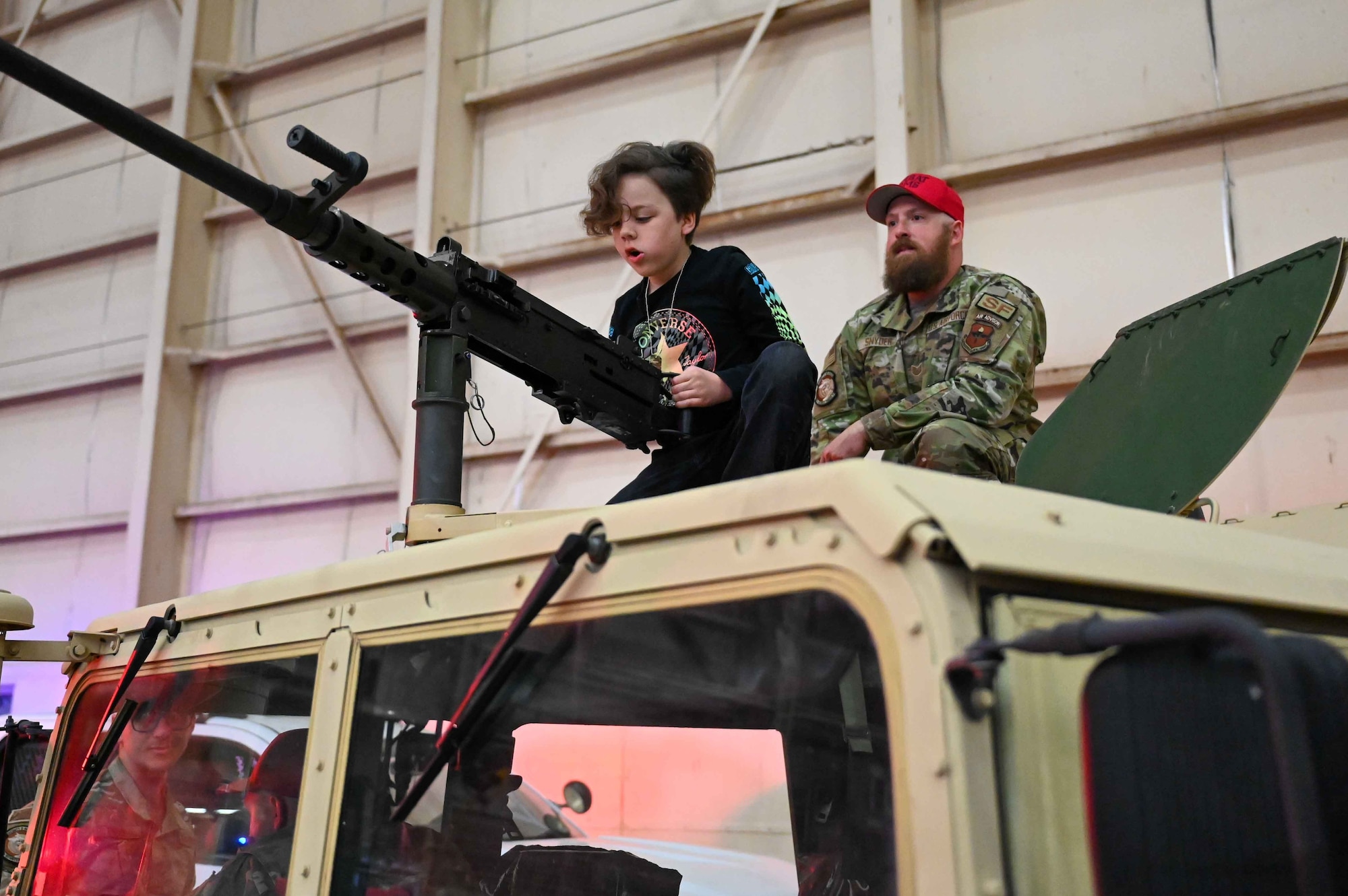 U.S. Air Force Tech. Sgt. Casey Snyder, 97th Security Forces Squadron combat arms noncommissioned officer in charge, watches a child get into the gunner position on a Humvee at Altus Air Force Base, Oklahoma, April 1, 2023. The goal of the “Kid’s Deployment Line” was to provide an immersive experience that represented each organization on the base. (U.S. Air Force photo by Airman 1st Class Kari Degraffenreed)