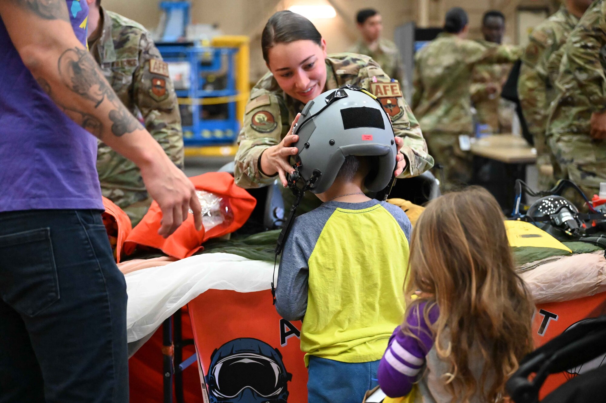 U.S. Air Force Airman 1st Class Heidi Phillips, 97th Operations Support Squadron aircrew flight equipment technician, adjusts a helmet on Nathanael Roldan, son of Staff Sgt. Cristhian Roldan, 97th Air Mobility Wing religious affairs noncommissioned officer in charge, during the “Kid’s Deployment Line” at Altus Air Force Base, Oklahoma, April 1, 2023. Airmen from the 97thForce Support Squadron’s Military and Family Readiness Center hosted the “Kid’s Deployment Line” to build resilience and understanding in the children of service members. (U.S. Air Force photo by Airman 1st Class Kari Degraffenreed)