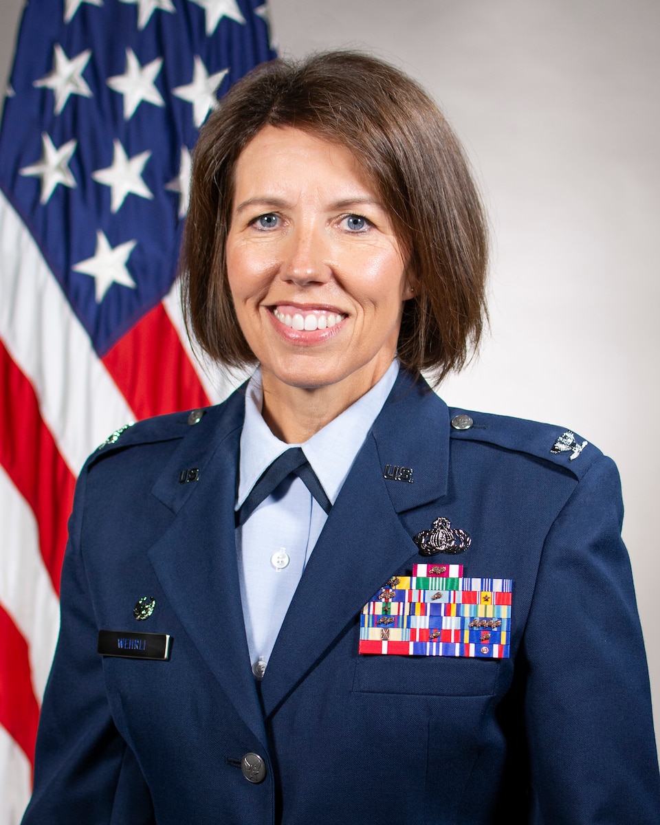 Service member smiles for an official photo in front of a U.S. Flag.