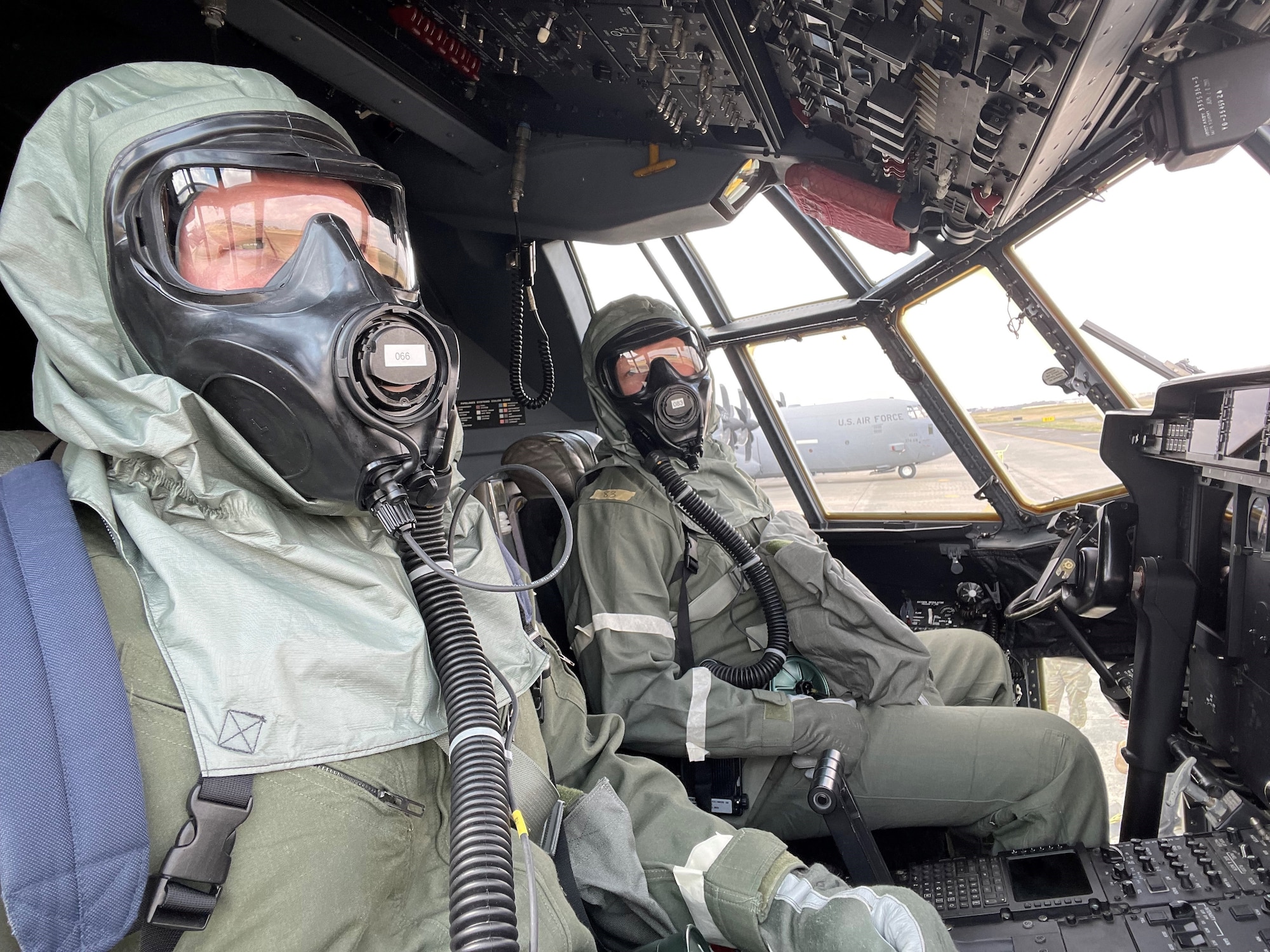 Two pilots in HAZMAT suits sit in the pilot seats of  a cargo aircraft