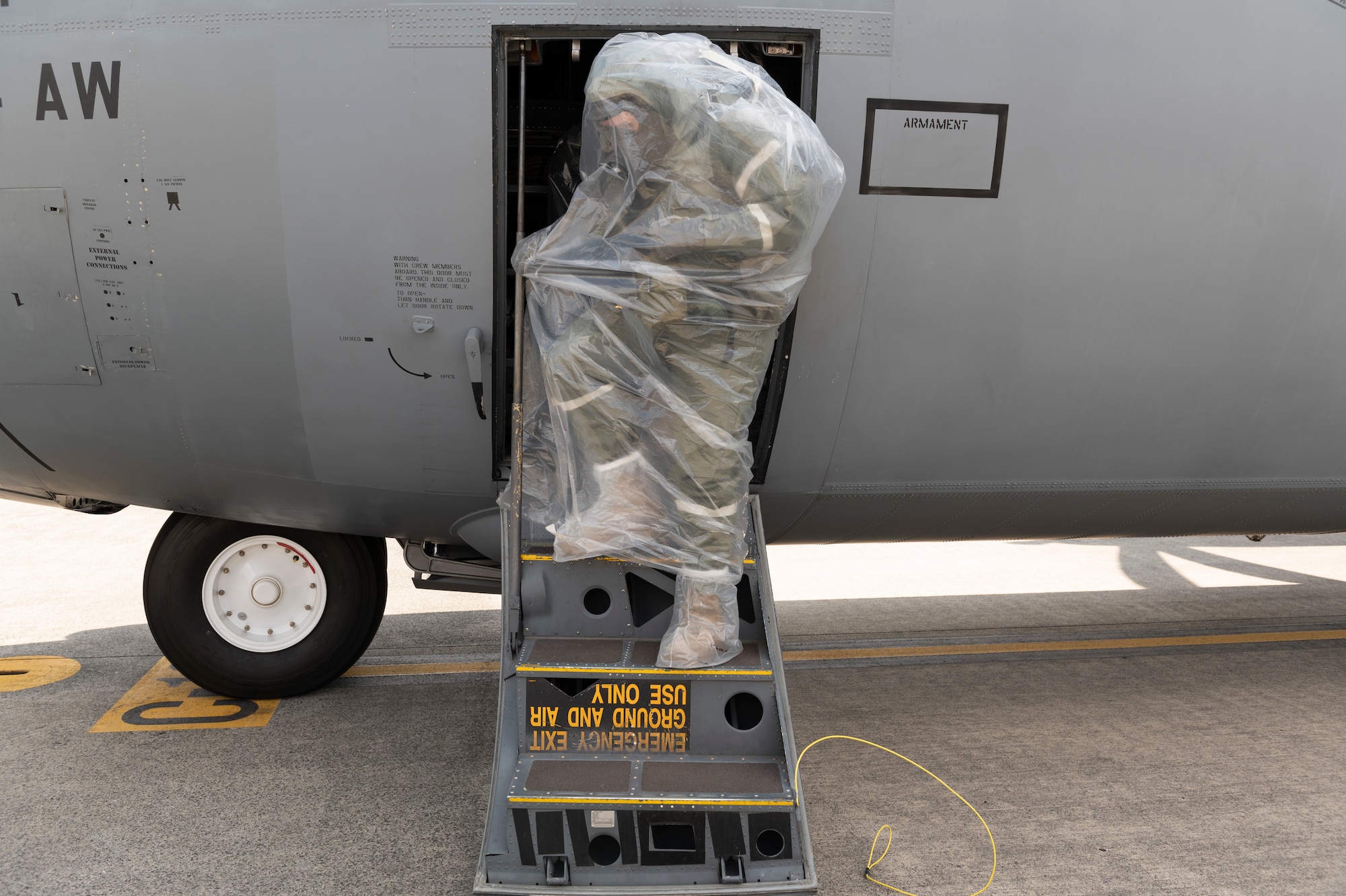 A pilot wearing protective gear and covered in a plastic bag steps out of a plane