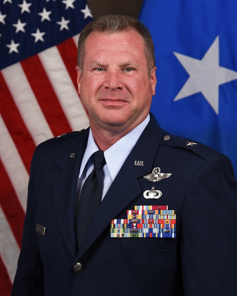 Service member poses for official portrait in front of U.S. Flag and one star flag.