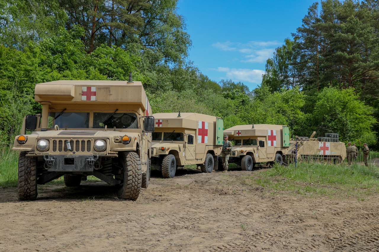 Military ambulances drive on a dirt road.