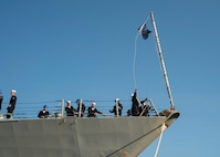 A Sailor aboard the guided-missile destroyer USS Nitze (DDG 94) raises the Union Jack as Nitze moors at Naval Station Norfolk after a scheduled deployment April 5, 2023.