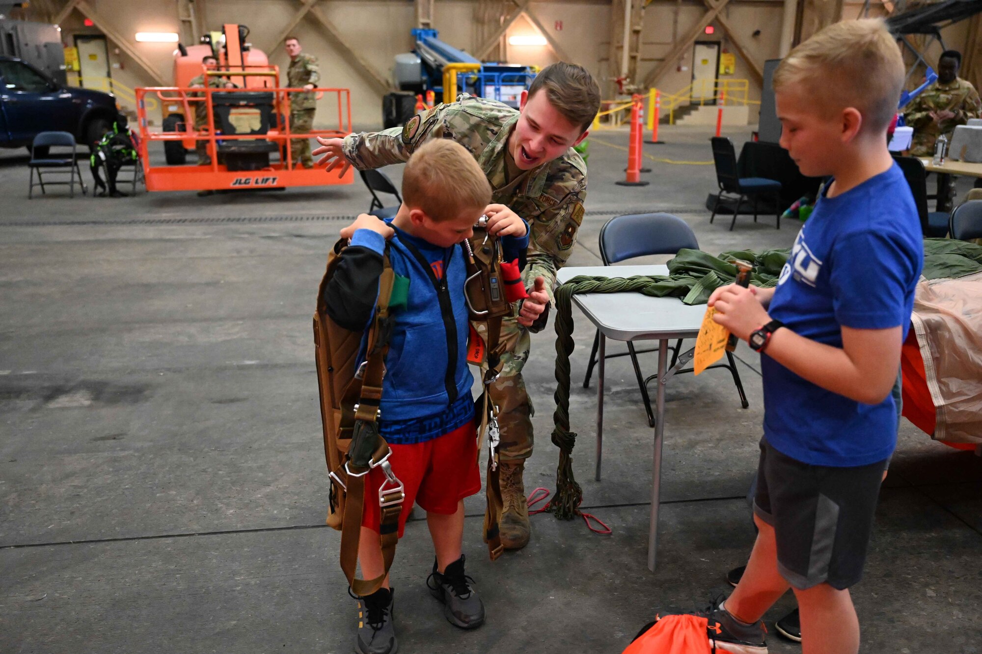 U.S. Air Force Senior Airman Brandon Schulze, 97th Operations Squadron aircrew flight equipment technician, places a parachute pack on a child during the “Kid’s Deployment Line” at Altus Air Force Base, Oklahoma, April 1, 2023. Over 160 Airmen and families attended the event. (U.S. Air Force photo by Airman 1st Class Kari Degraffenreed)