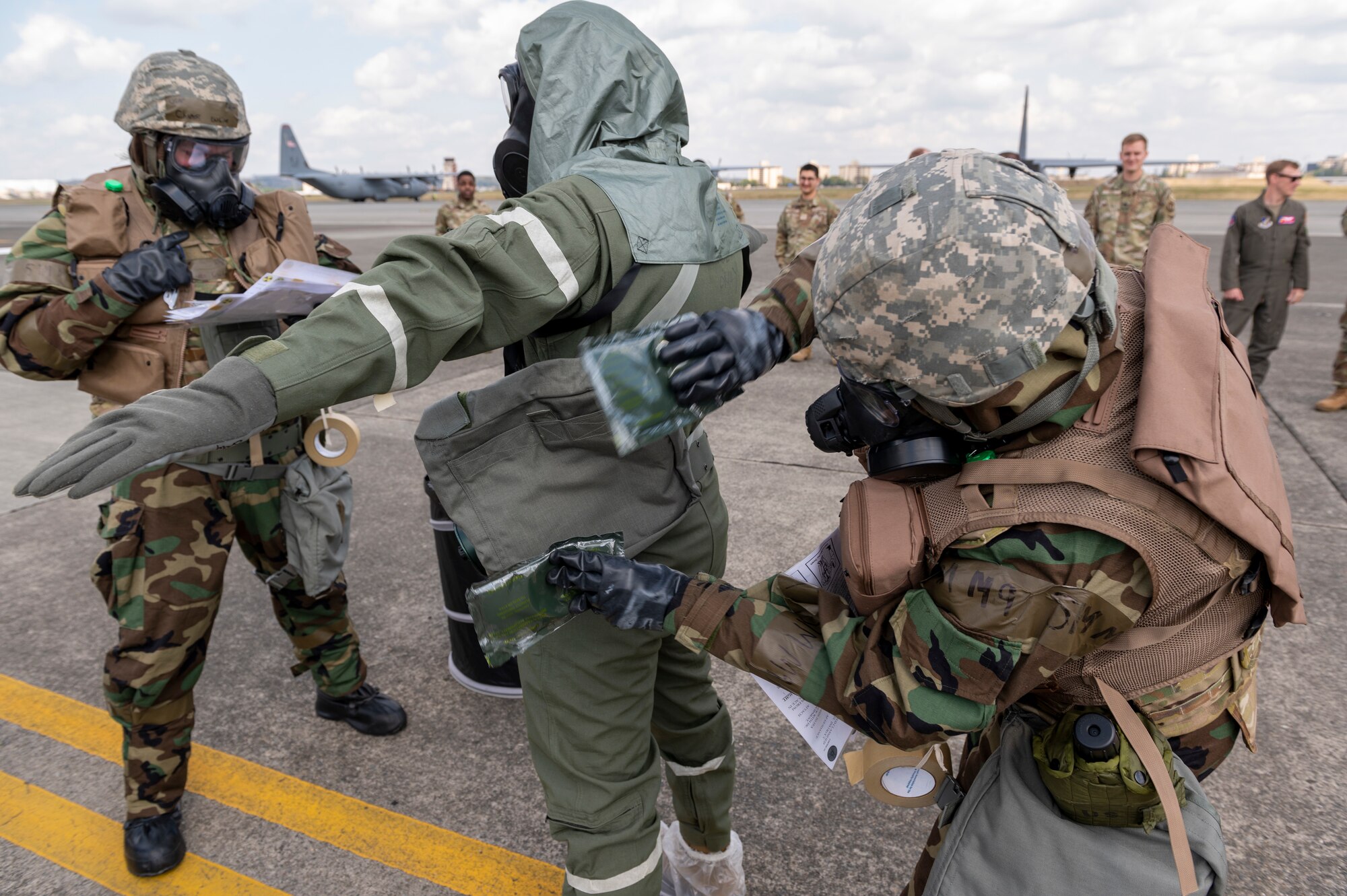 Two airmen wearing protective gear pat down a pilot also wearing protective wear
