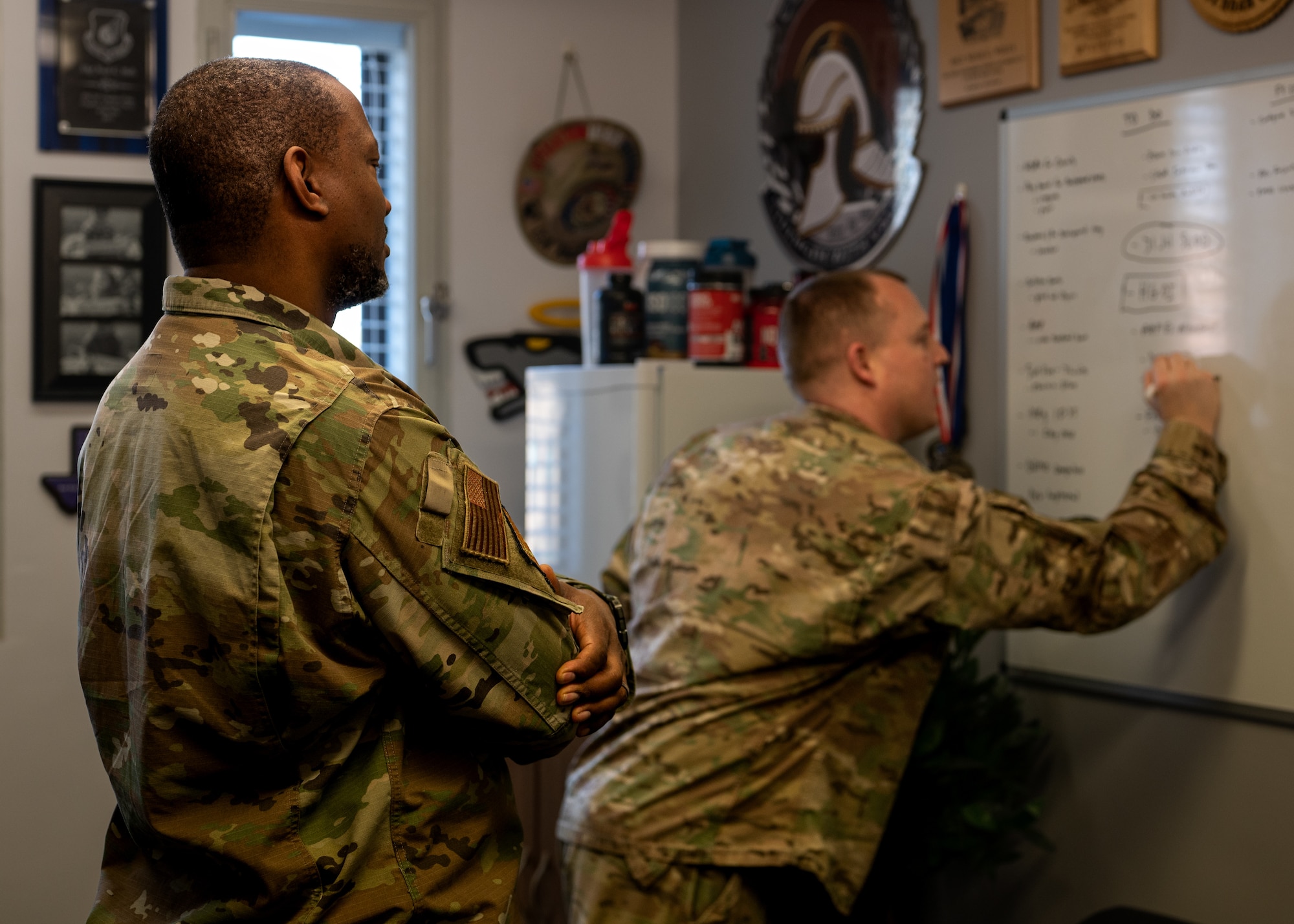 U.S. Air Force Tech. Sgt. Dundre Davis, Liberty Wing Chapel noncommissioned officer in charge of programs and administration, watches Master Sgt. Noah Wells, Religious Affairs superintendent, make notes on his whiteboard at Royal Air Force Lakenheath, England, April 3, 2023.
