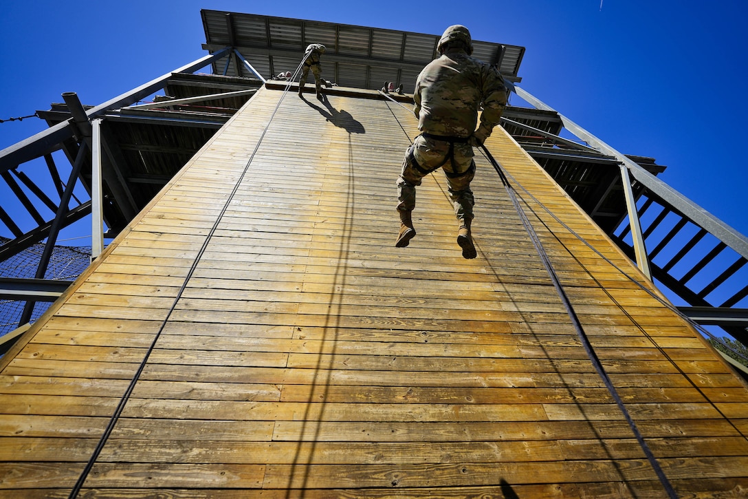 Soldiers rappel down a wooden tower.