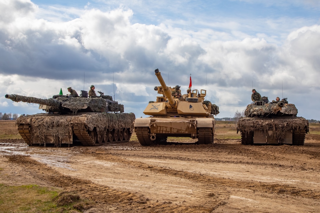 Three military tanks are parked in a muddy field.