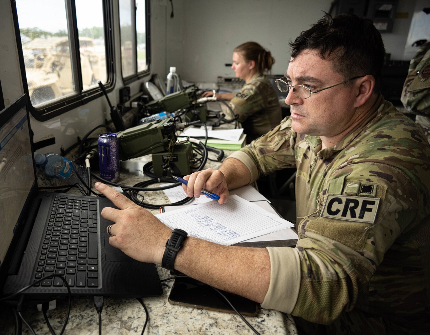 Airman speaks into 2-way radio sitting at a desk.
