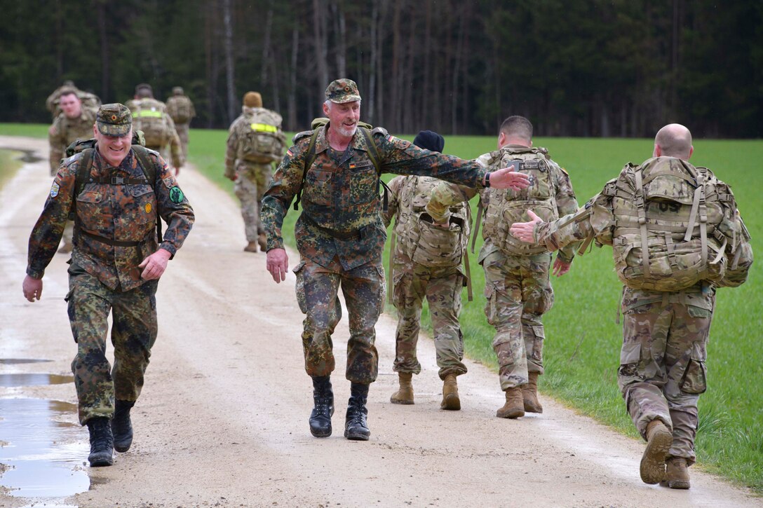 A U.S. and a German soldier high-five while walking in opposite directions on a trail as fellow service members walk nearby.