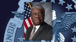 Milton Lewis. A dark skinned man in a dark grey business suit. This is a headshot.