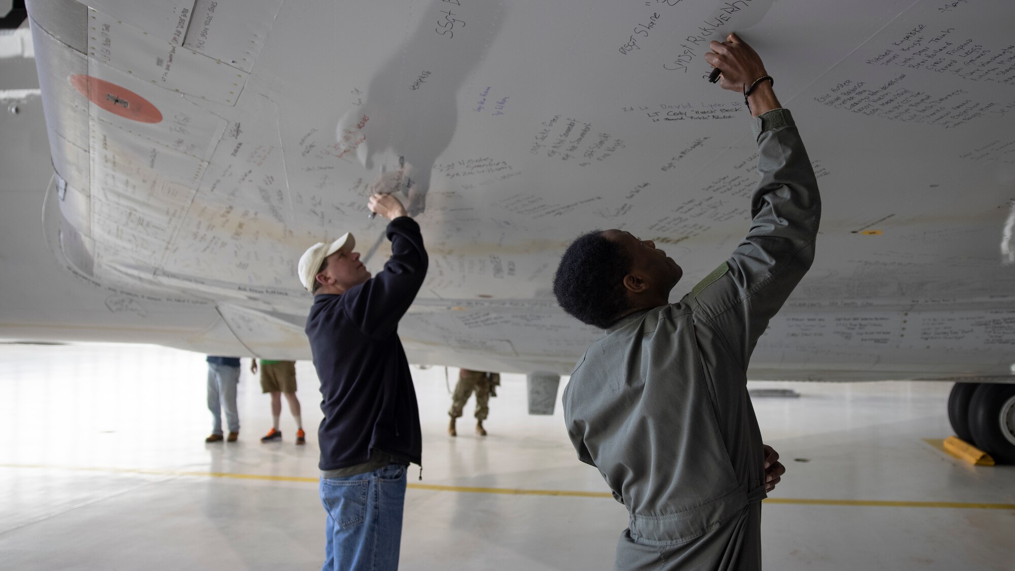 Two men (one Civilian, one Military) signing the underside of a wing