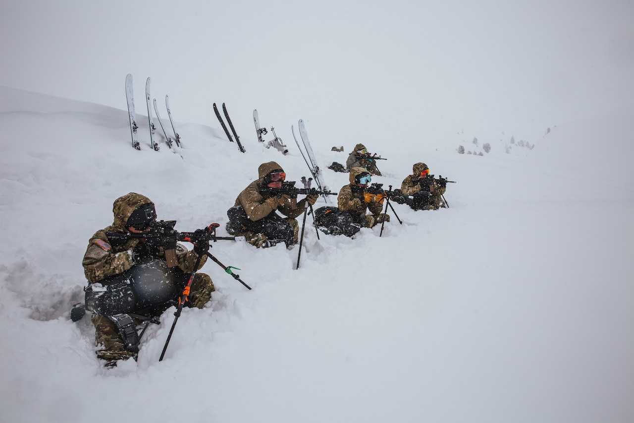 Soldiers sit in the snow and aim weapons.