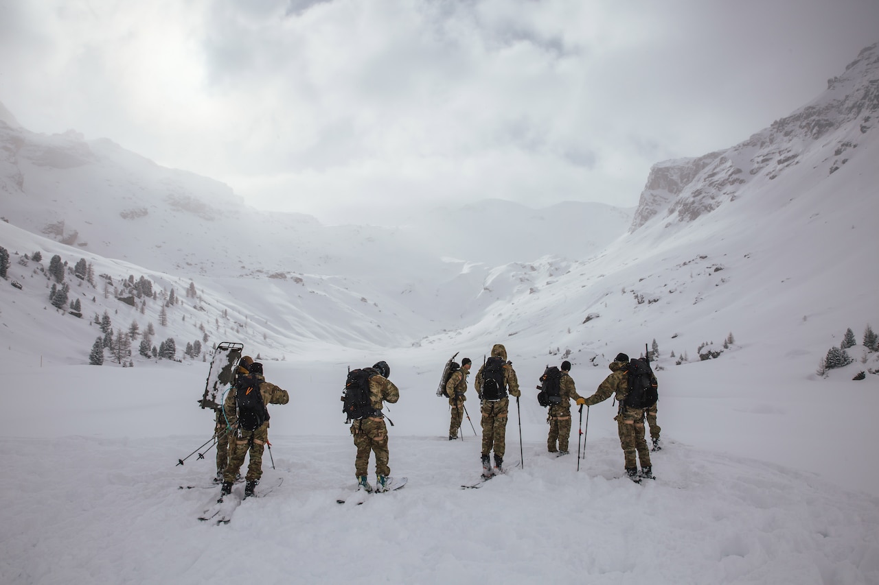 Soldiers move on skis in mountainous terrain.