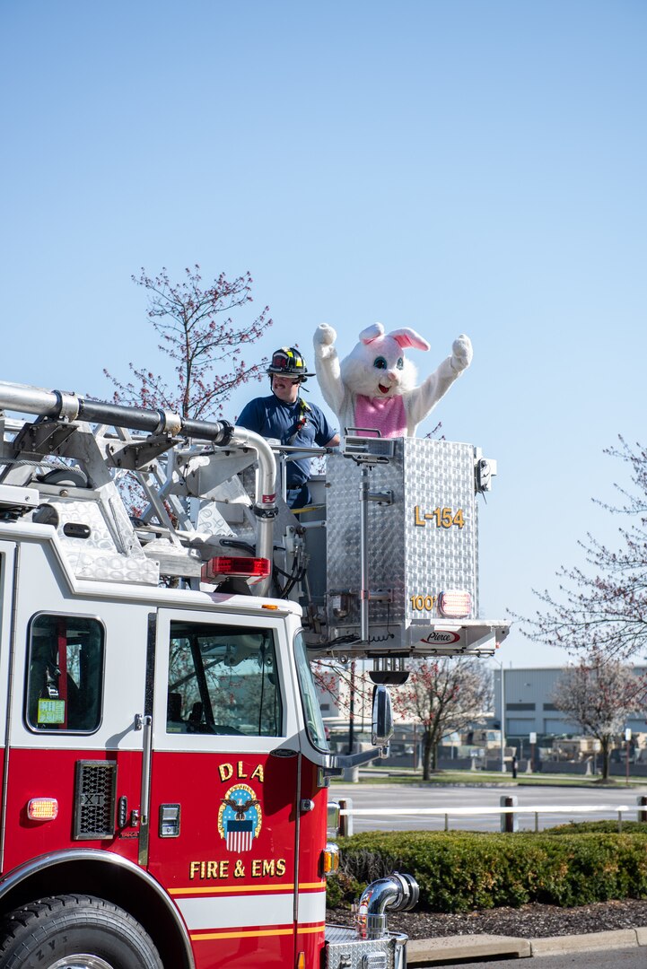 A person dressed as the Easter Bunny waves from the bucket of a red ladder truck.