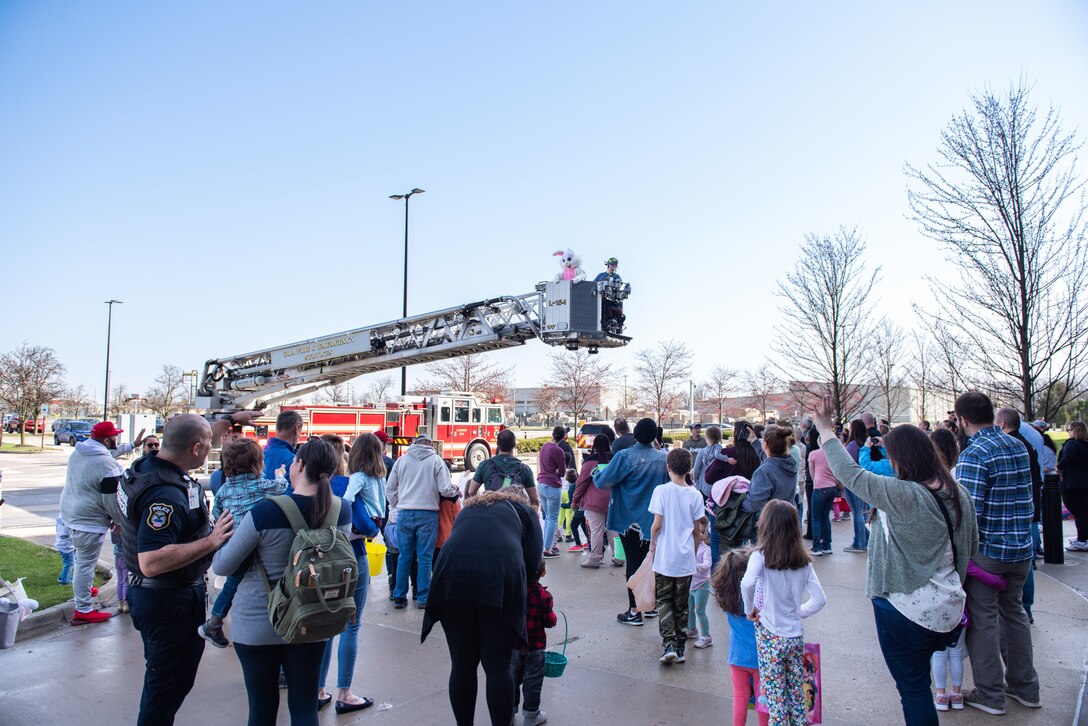 A person dressed as the Easter Bunny waves from the bucket of a red ladder truck.