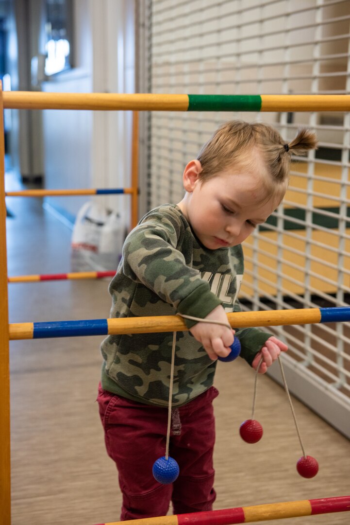 A small child untangles ropes with colorful balls attached from a horizontal post.