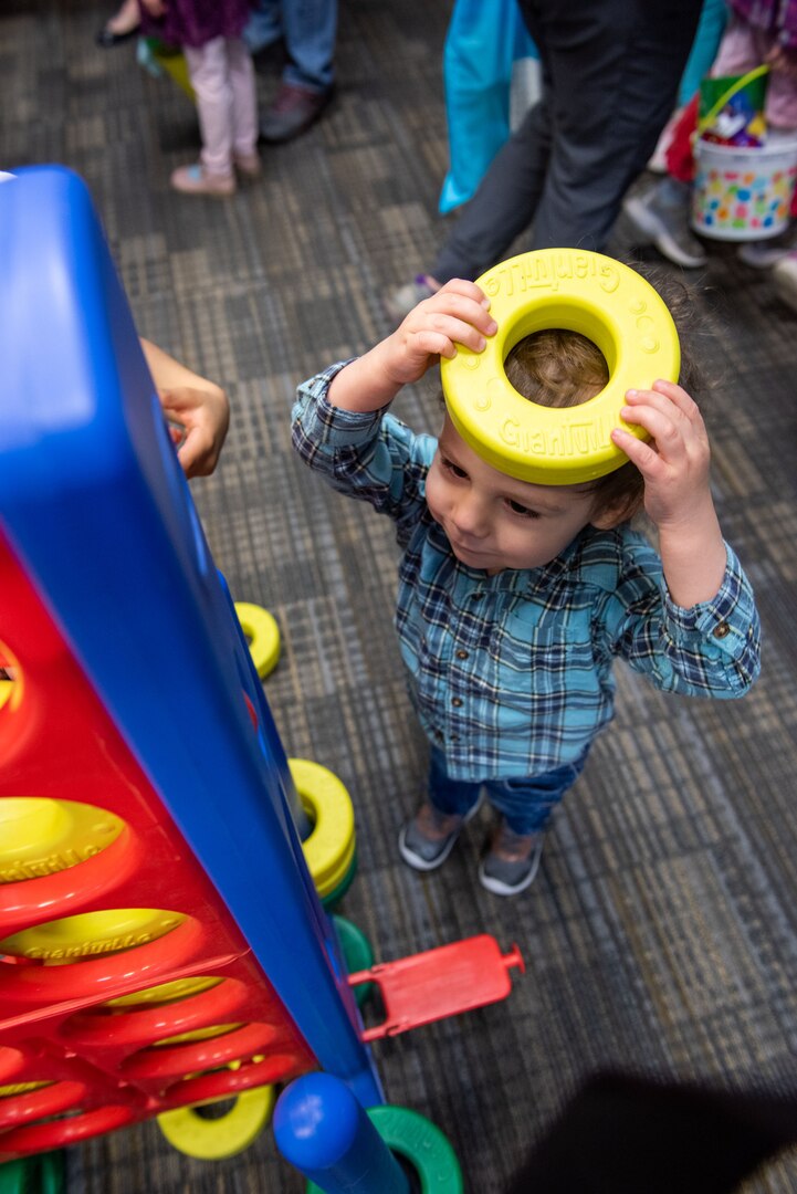 A little boy holds a bright yellow and round Connect Four game piece on his head.