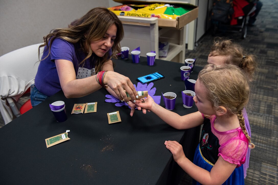 Children receive seeds to plant flowers from a woman in a blue shirt at a table.