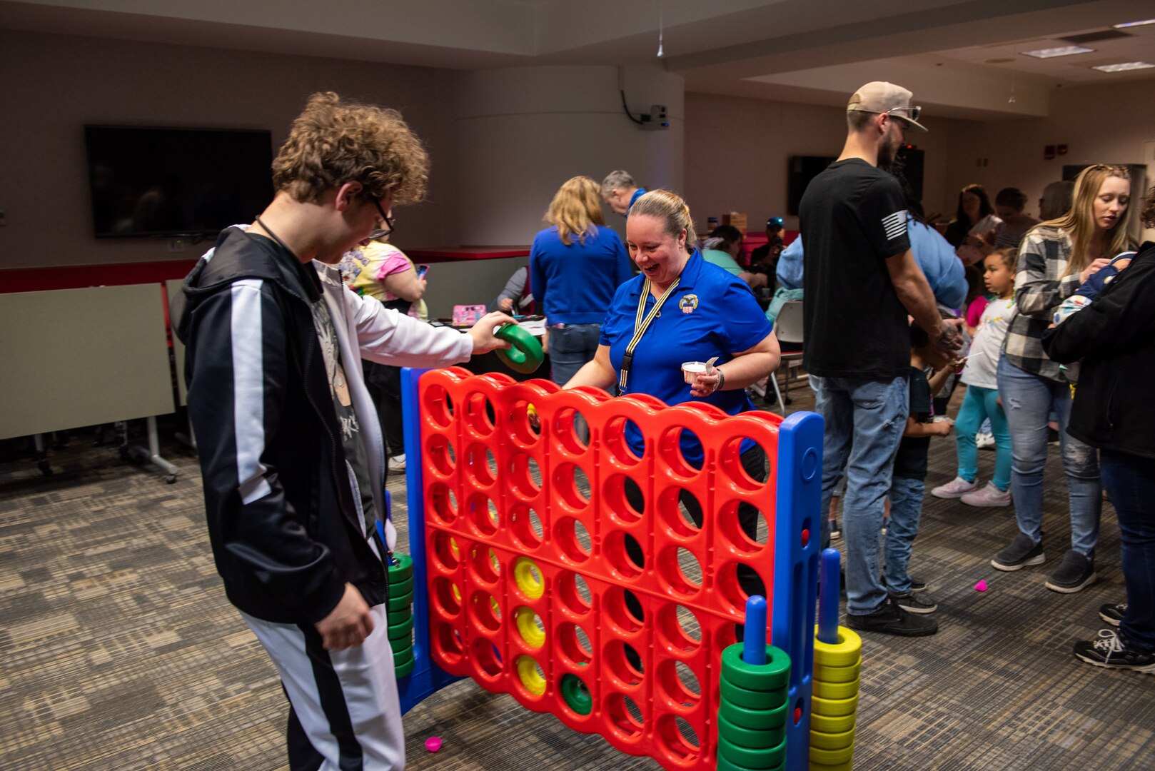 Several people play a life size Connect Four game inside a room. with grey carpet.
