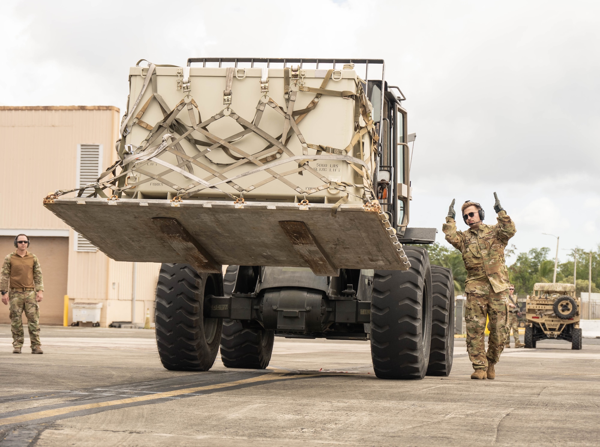 Airman directs a forklift carrying a pallet toward an aircraft on the flight line.