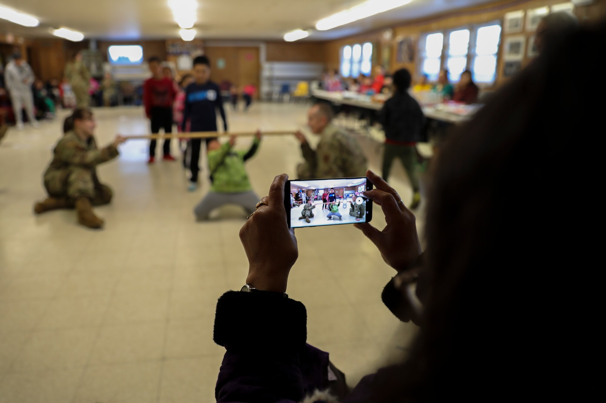 A community member captures an image of Tech. Sgt. Brittany Wright, an Alaska Air National Guard recruiter with the 176th Wing, left, and Master Sgt. Michael Thomas, incoming Recruiting and Retention superintendent for the Alaska Air National Guard, holding a limbo stick as community members participate in a game night at the City Hall in St. Mary’s, Alaska, March 31, 2023. The local girls club, the Roses of Andreafski, sponsored the community event inviting the Guardsmen to join in the festivities.