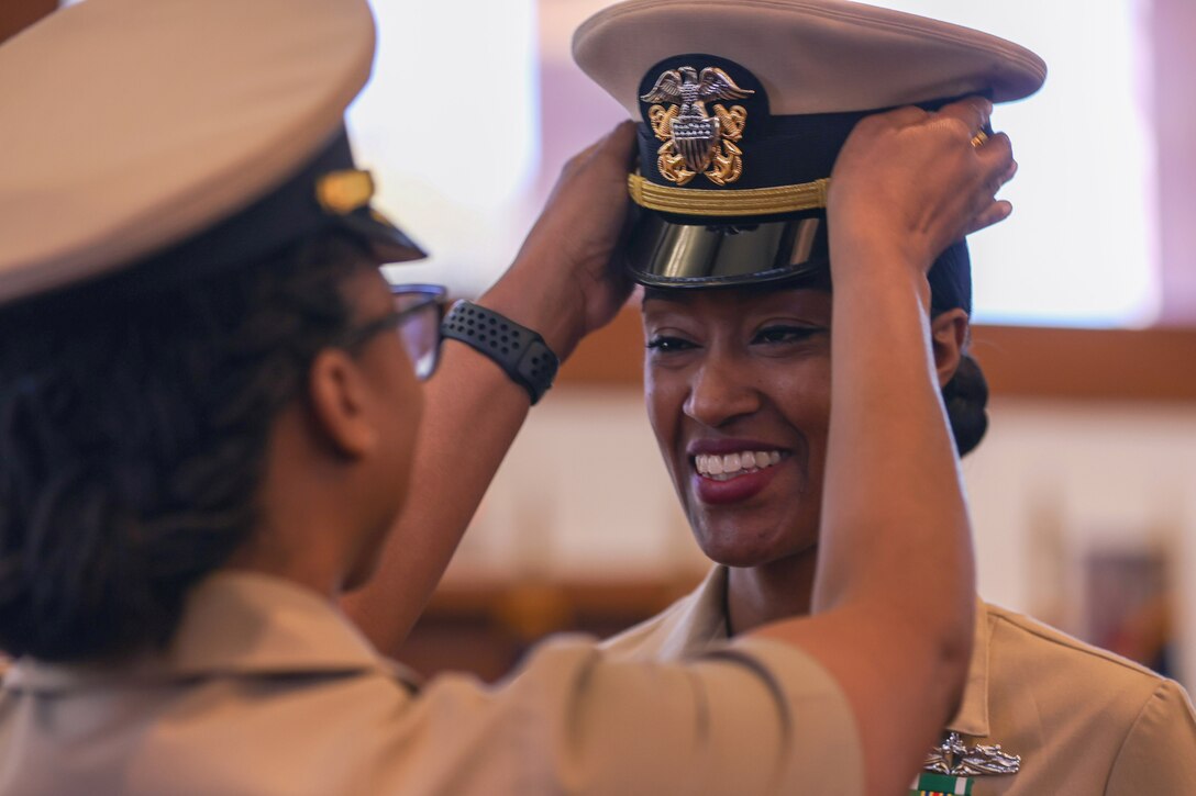 A sailor smiles as a cap is put on her head.