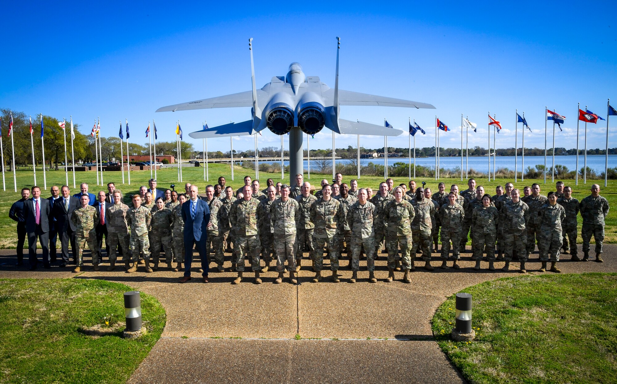 Group of people stand in formation for a group photo in front of an F-15 static display.