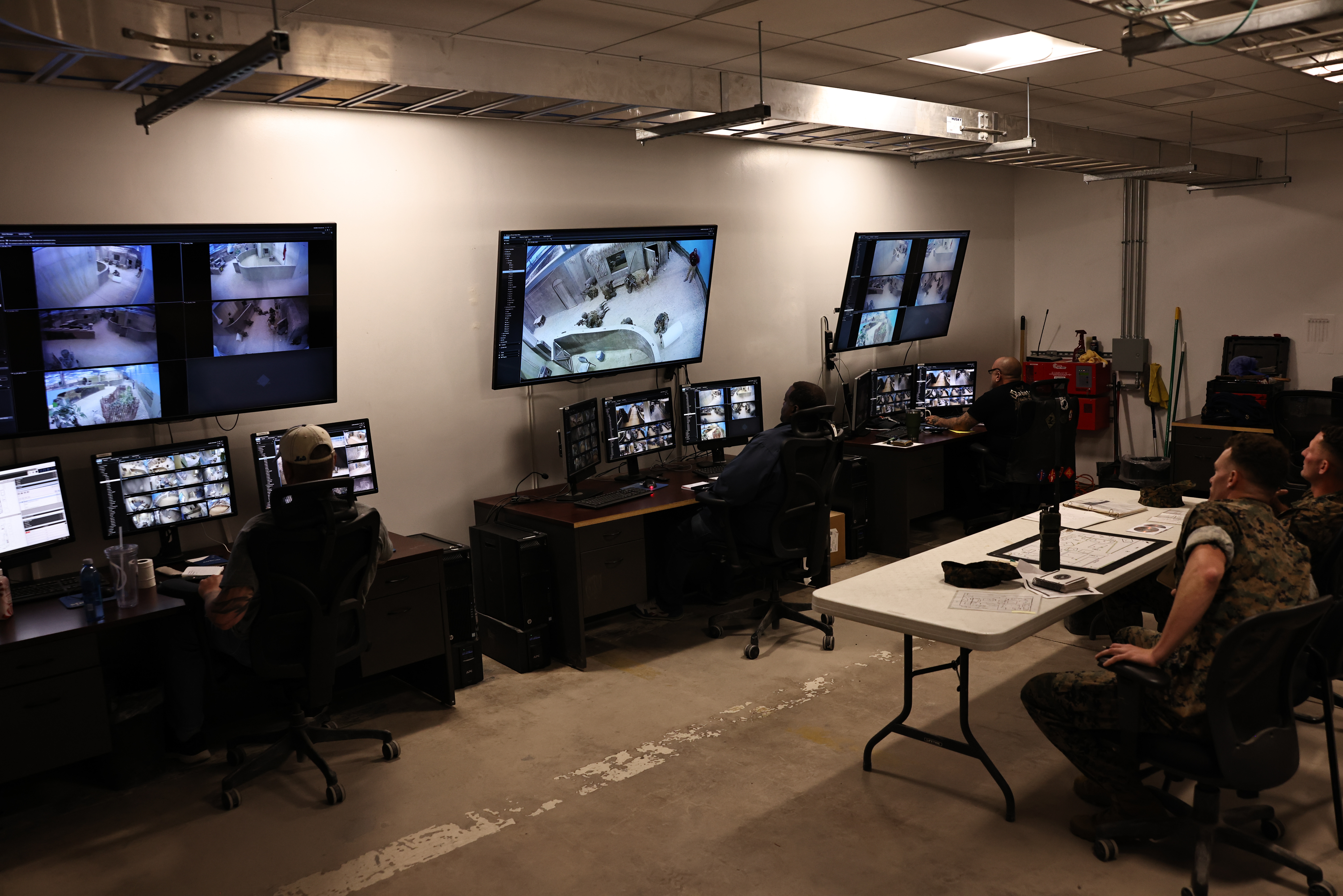 Marines in a camera room with multiple monitors on the wall.