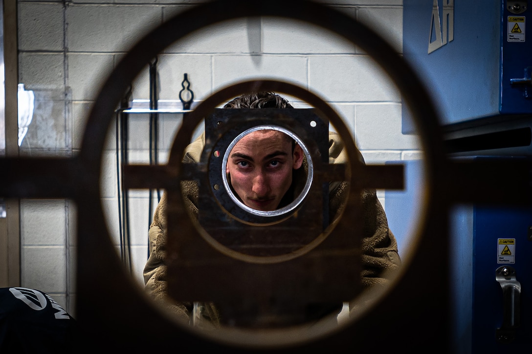 An airman looks through the opening of a metal fixture.