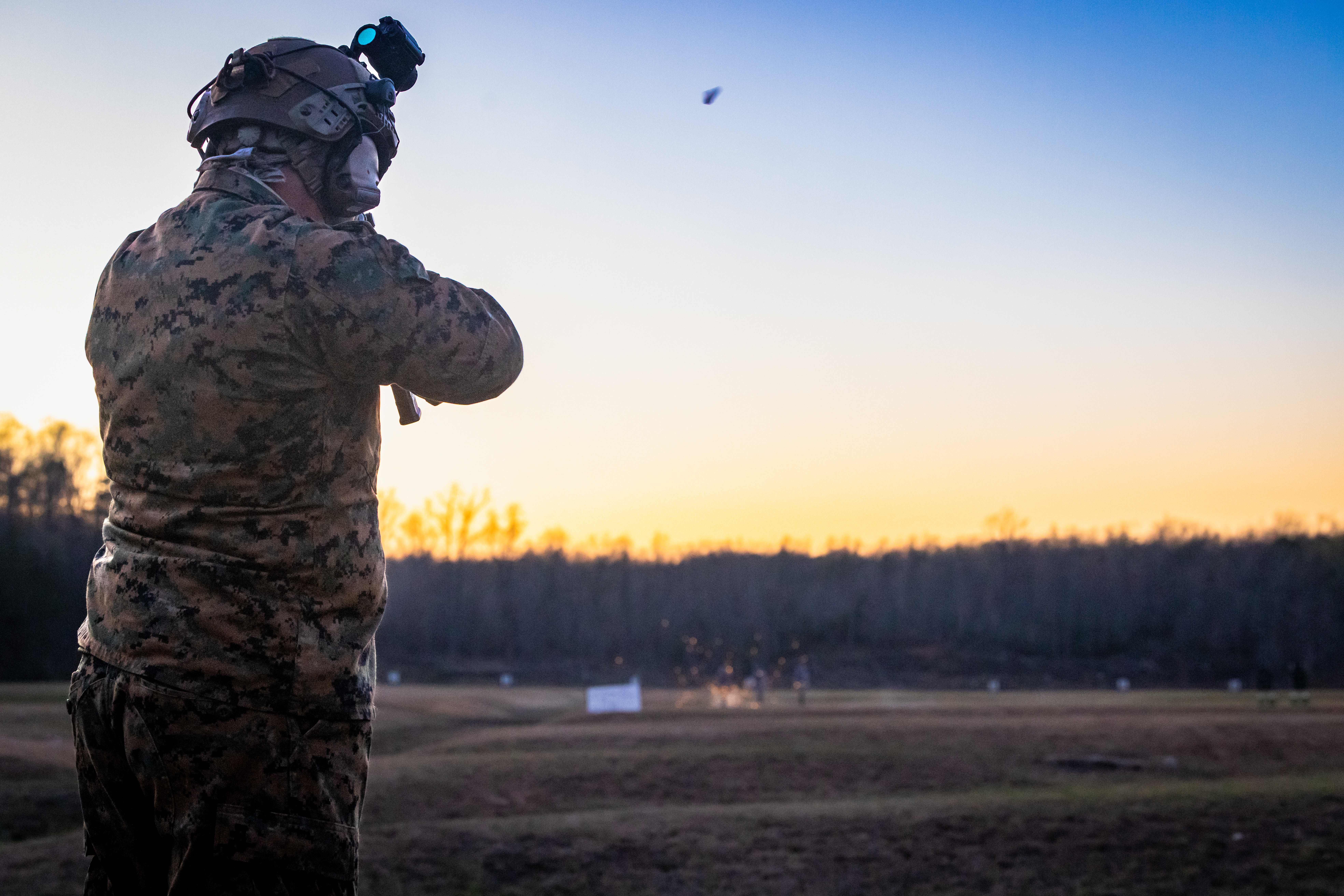 A Marine in combat uniform, aiming a gun while facing the sunset.