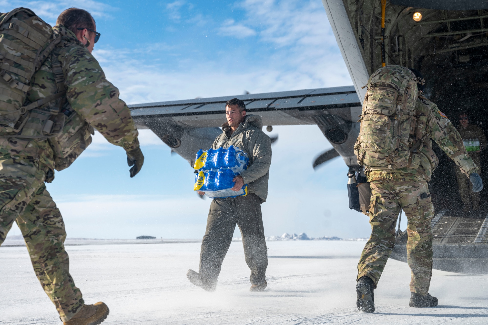 A loadmaster carries a case of water from a C-130J Super Hercules